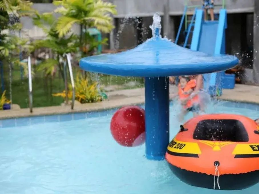 Blue mushroom fountain pouring water into the shallow kids' pool, with an inflatable boat and ball